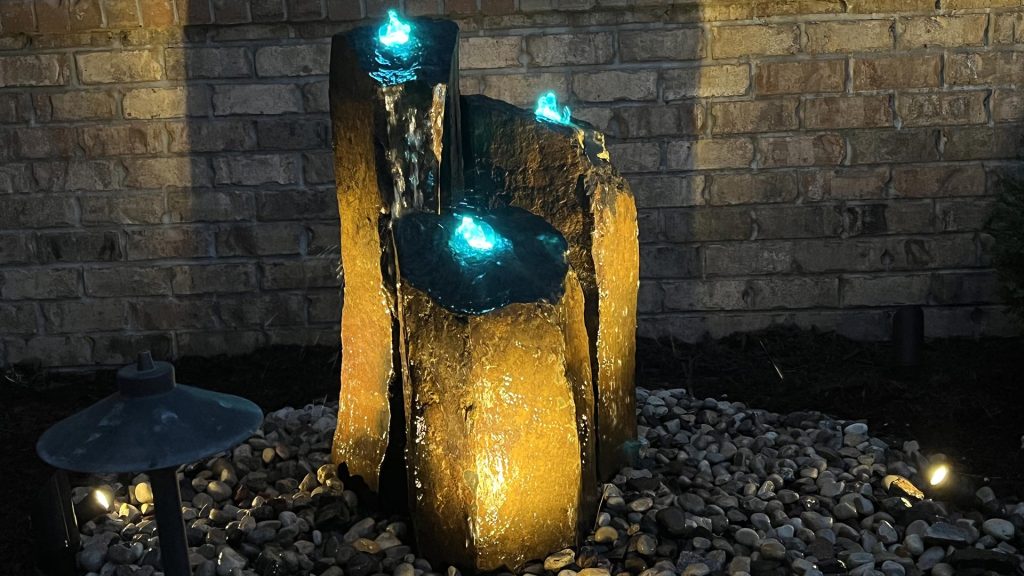 Accent lighting illuminating a stone water feature at night