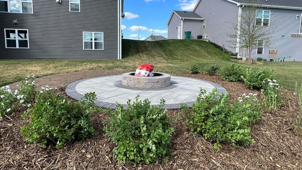 Built-in circular fire pit centered in a paver gathering area with landscape planting