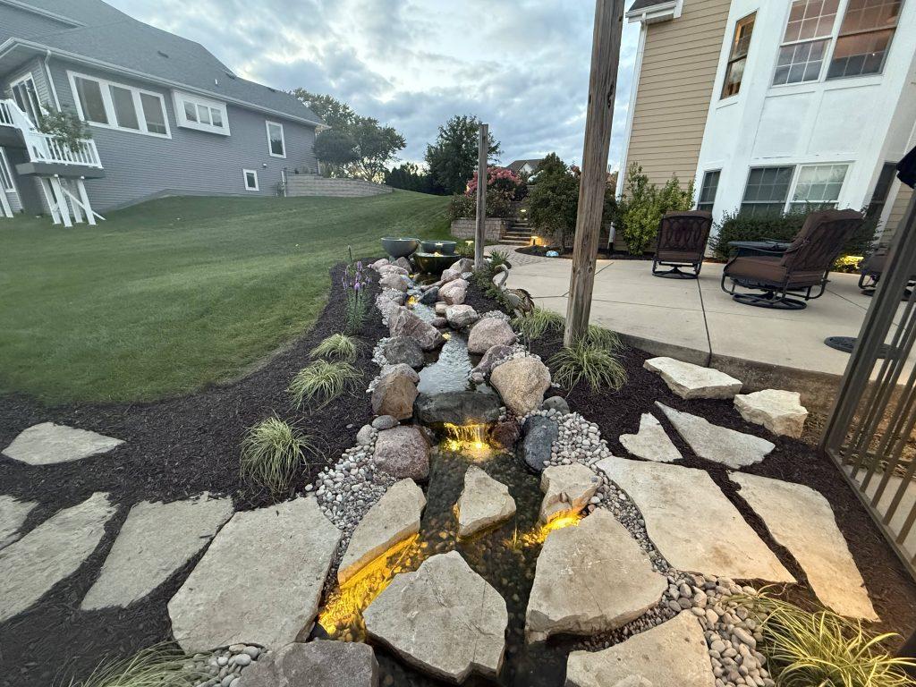 Rock-lined cascading water feature beside a patio and landscape planting